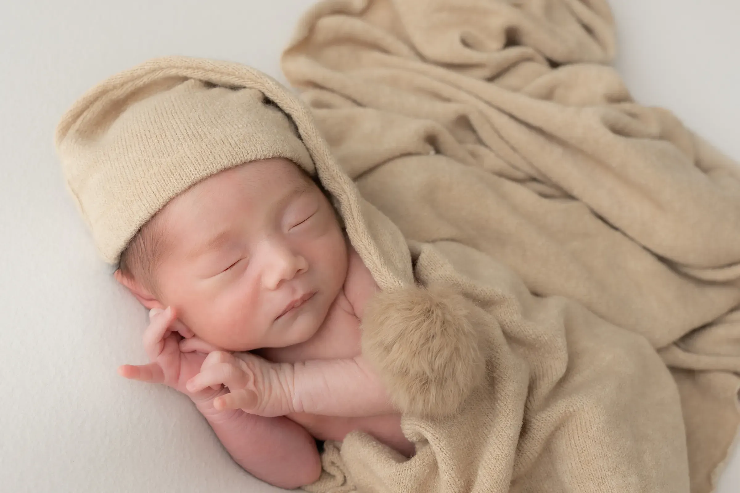 ベージュのニット帽とブランケットで眠る赤ちゃん