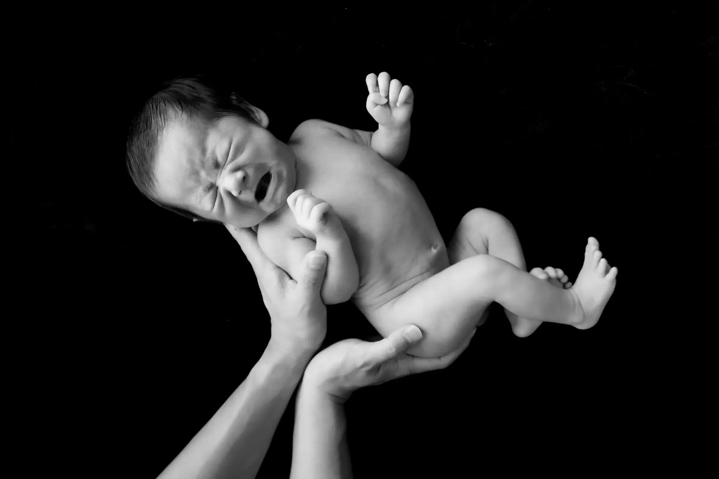 黒い背景で、大人の両手に持ち上げられる赤ちゃん（モノクロ）