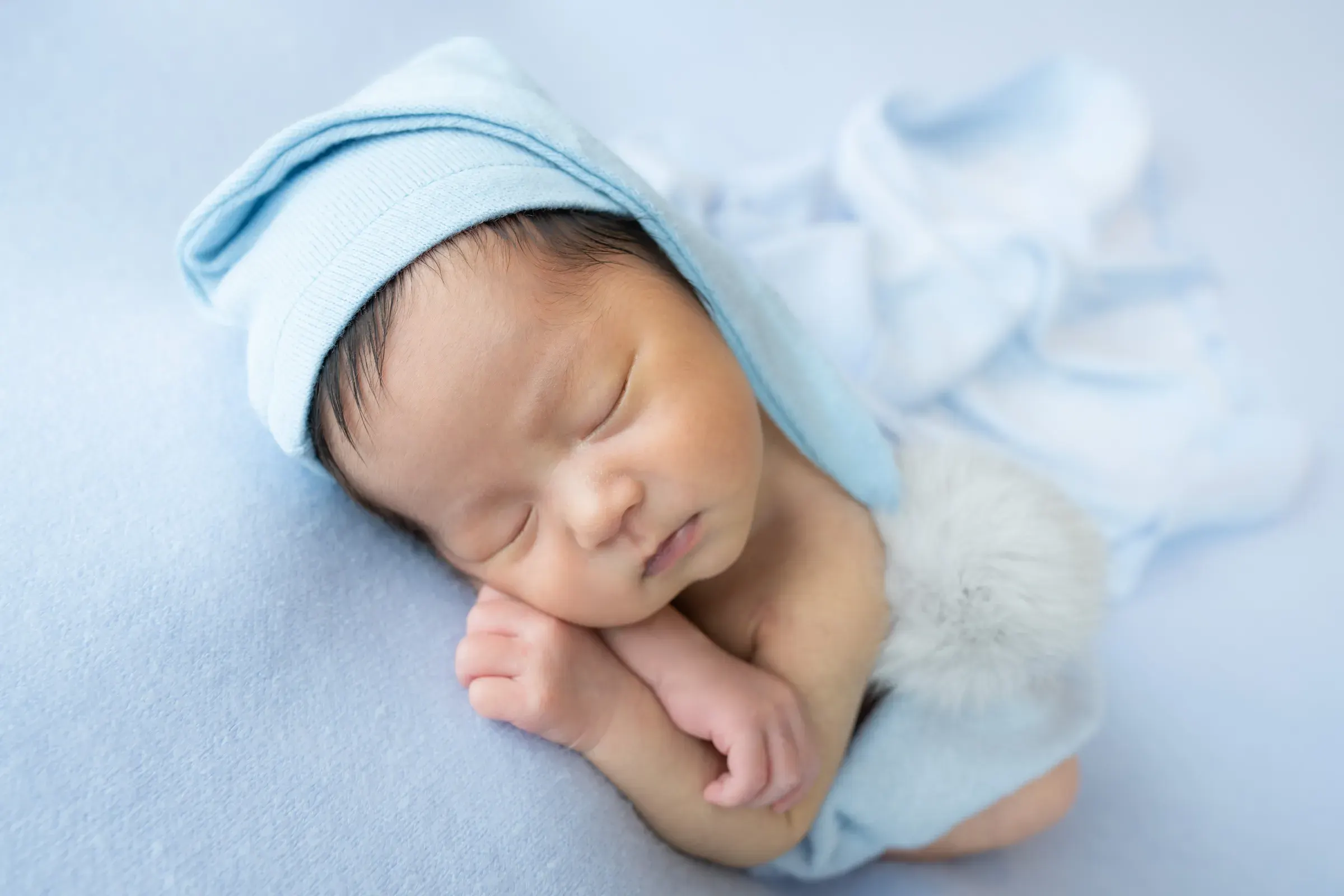 水色のニット帽をかぶり、水色の背景で眠る赤ちゃん