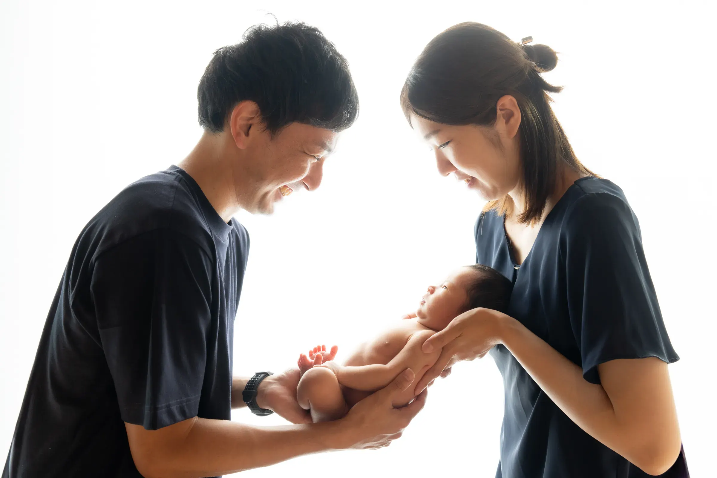 向かい合って笑顔で赤ちゃんを抱き上げるパパとママ