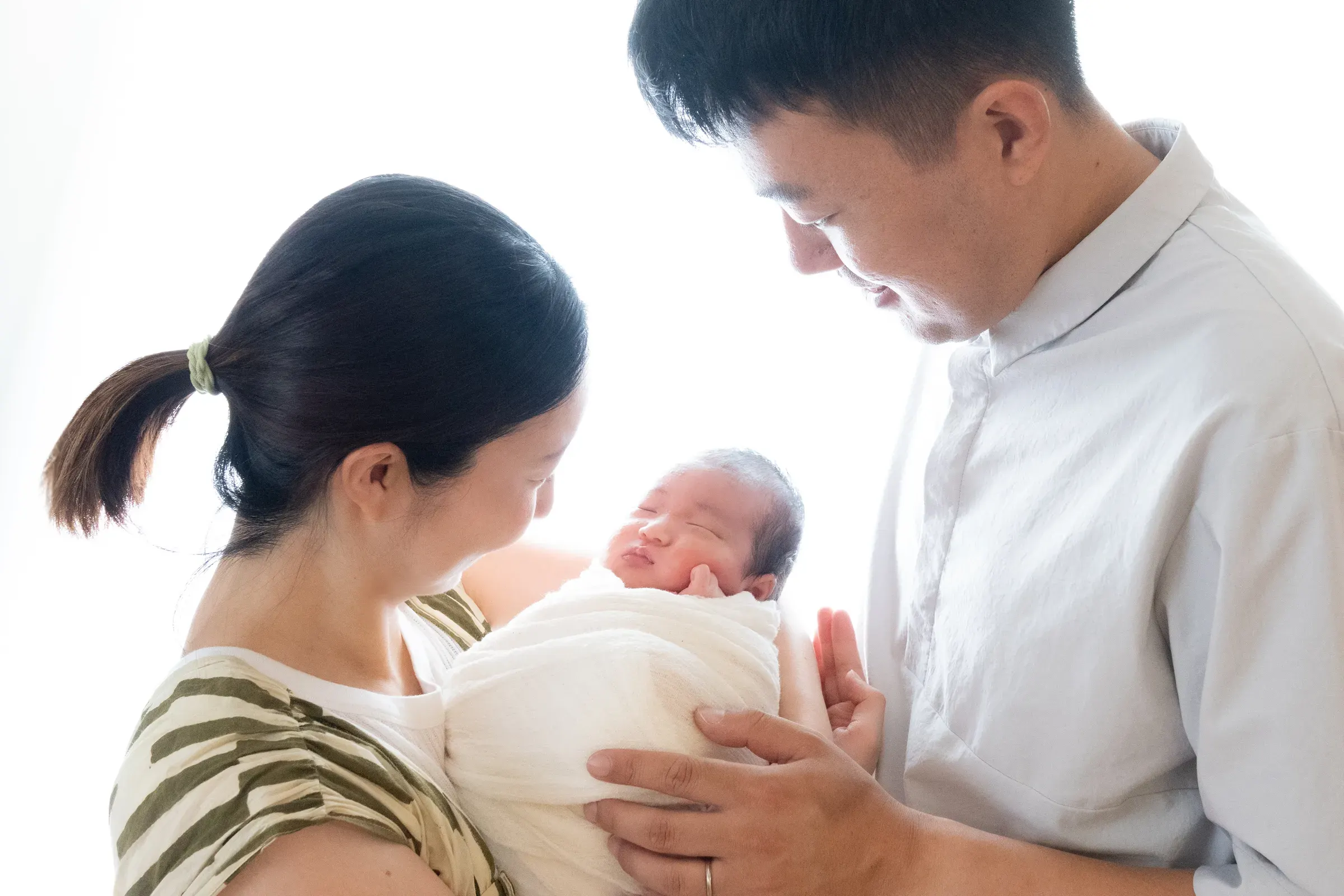 生まれたばかりの赤ちゃんを抱き、やさしく見つめるパパとママ（モノクロ）