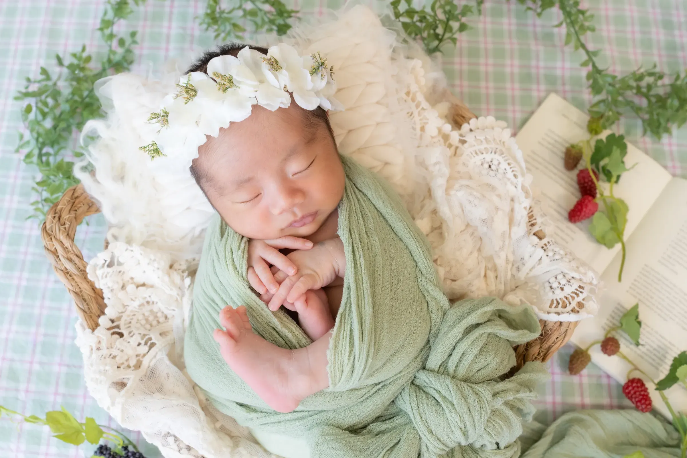 グリーンのおくるみに包まれ、花冠をつけて籠の中で眠る赤ちゃん