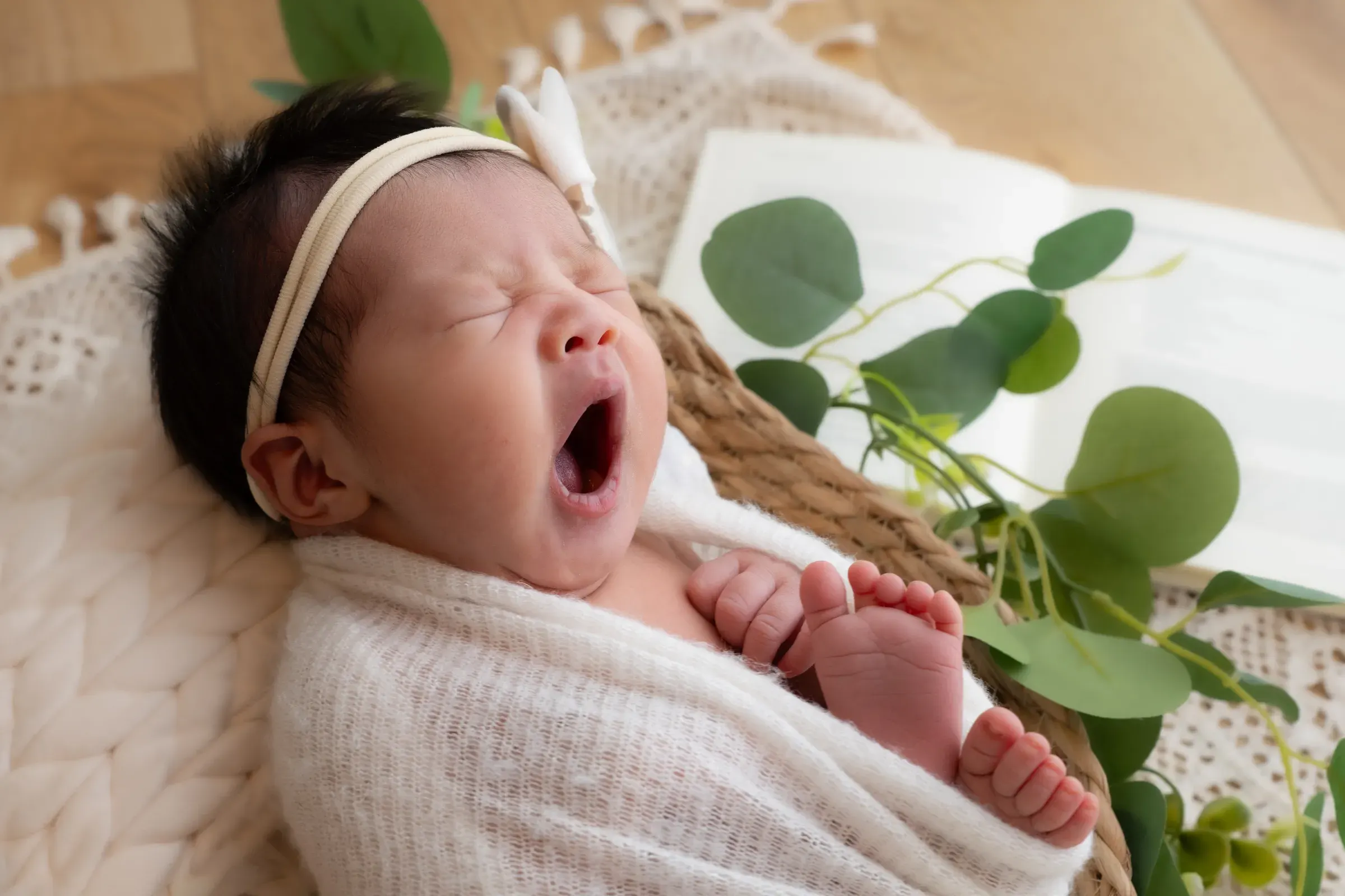 白いおくるみに包まれ、大きくあくびをする赤ちゃん